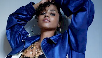 Tyla posing in a shiny jacket with her hands over her head